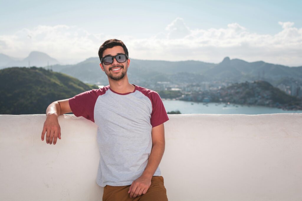 pexels-photo-1121796-1121796 Young man in sunglasses leaning on a balcony with a scenic city view in the background.